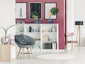 Pink feature wall with bookshelf and chair and wooden table with plants and lamps with exposed brick